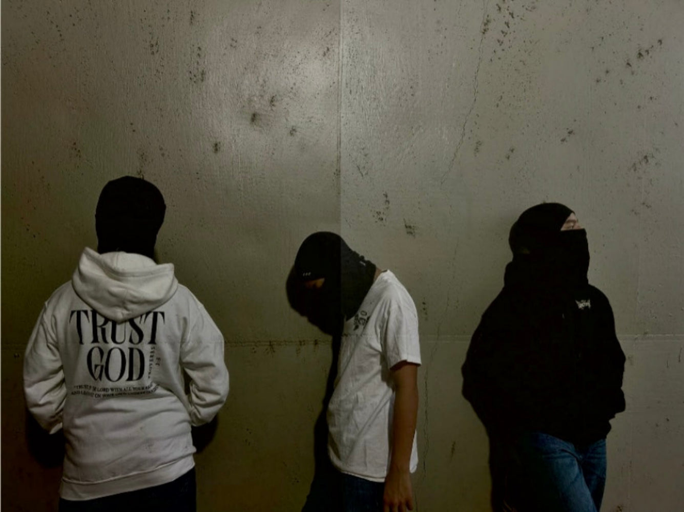 Three individuals wearing hoodies with text against a textured wall.